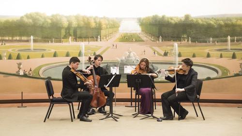 A string quartet performing in front of a large mural depicting a classical garden scene. The players are deeply engaged in their music. 设置, highlighted by the grand mural of a baroque garden with neatly trimmed hedges and statues, adds a formal and historic ambiance to their performance. The musicians, dressed in concert attire, enhance the elegant and artistic atmosphere of the scene.