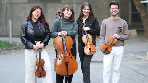 string quartet members standing outside and posing for photo behind a building